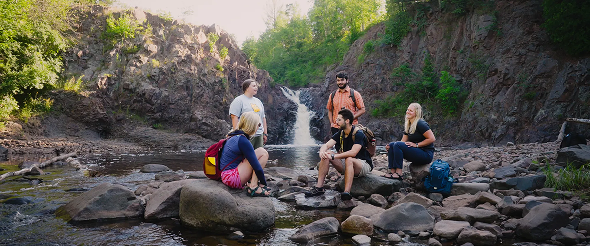 five students conversing with waterfall in background