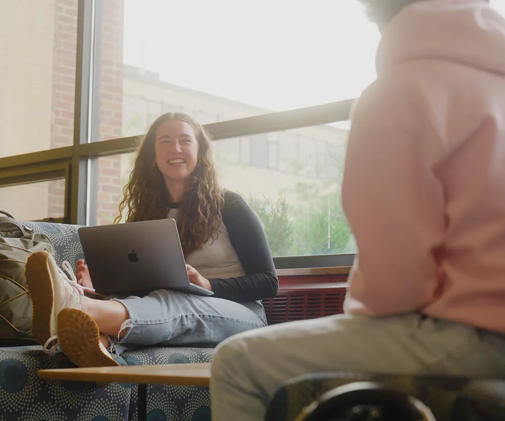 two students laughing inside on campus.