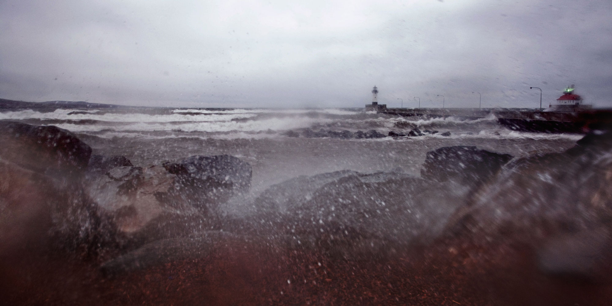 Waves roll in from Lake Superior during a storm with the Duluth entry lighthouse in the background.