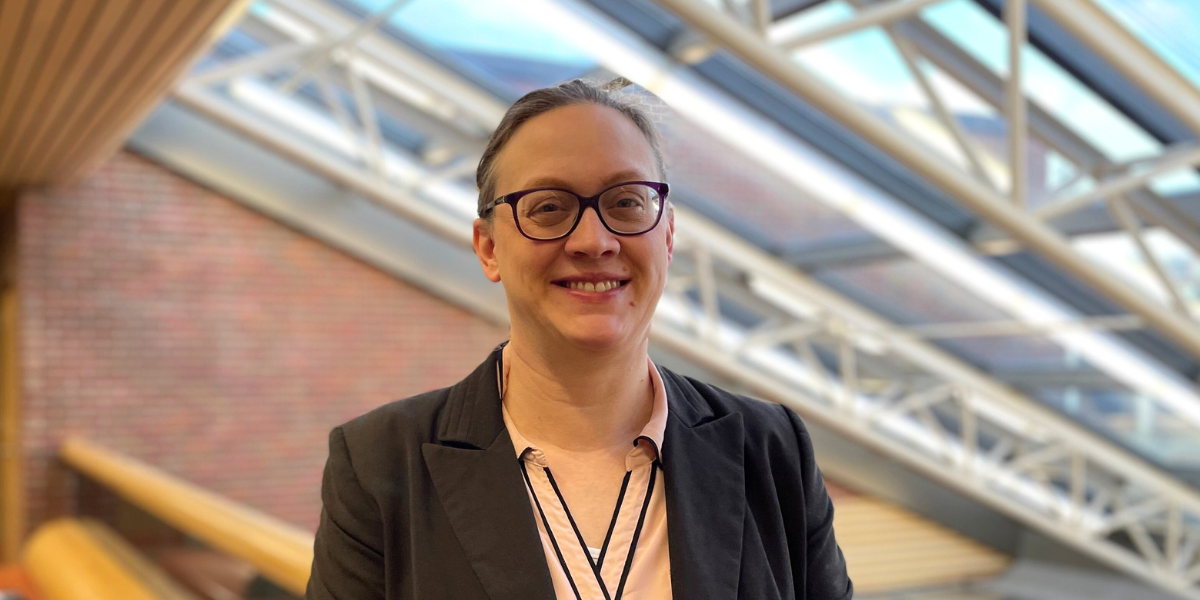Jessica Hanson, smiling with hair pulled back and wearing glasses and a dark blazer