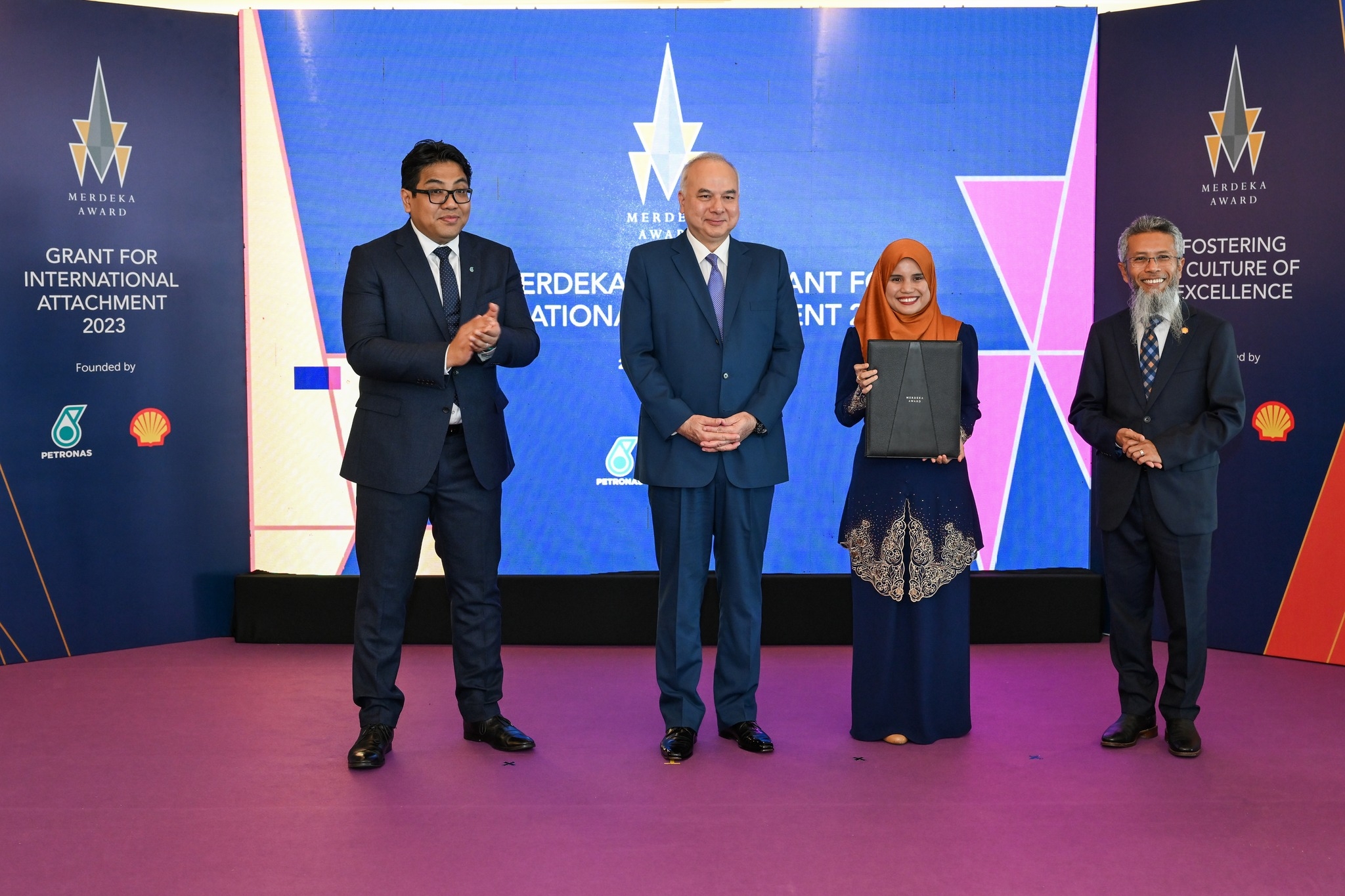 Four people on a colorful stage, Syaza is accepting the Merdeka Award